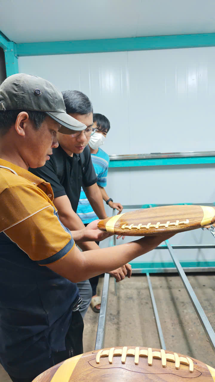 Người vận hành cầm kiểm tra bề mặt khay gỗ hình quả bóng bầu dục sau khi phun sơn