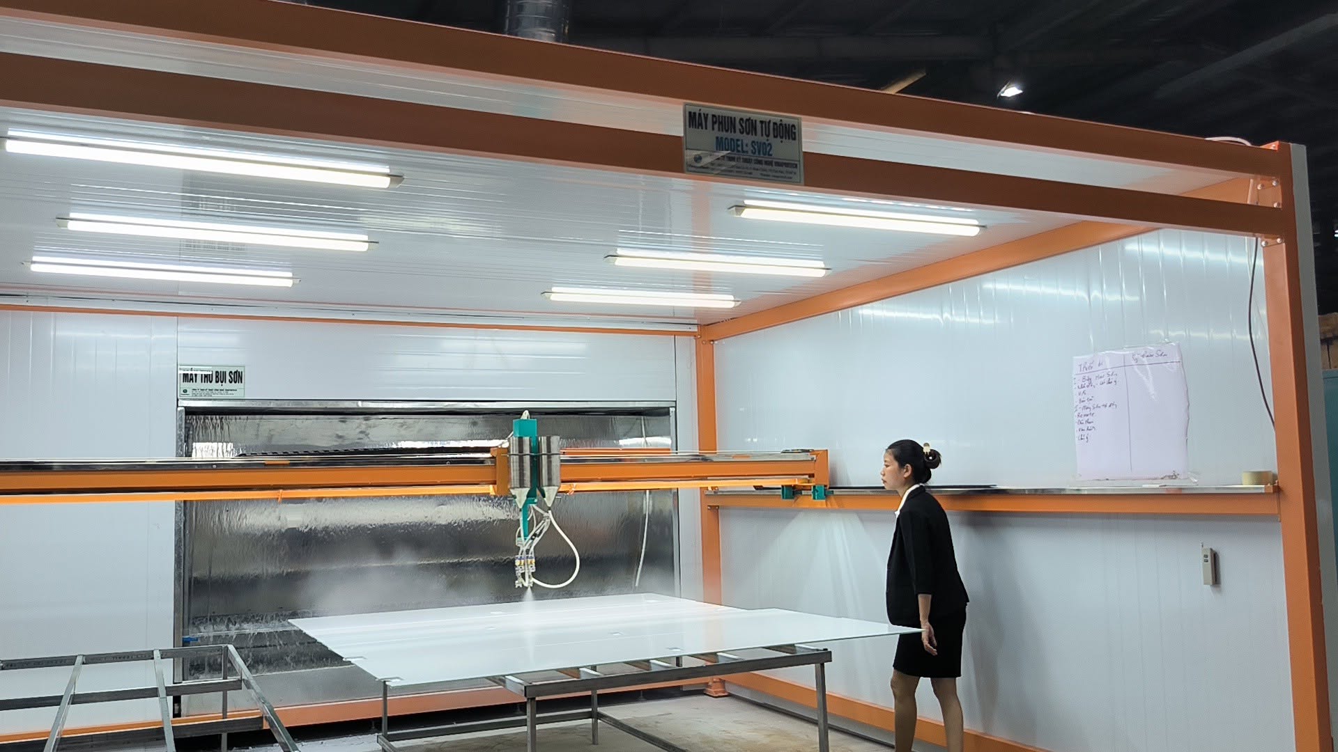 Khu vực lắp máy phun sơn với khung màu cam và bàn đỡ phôi