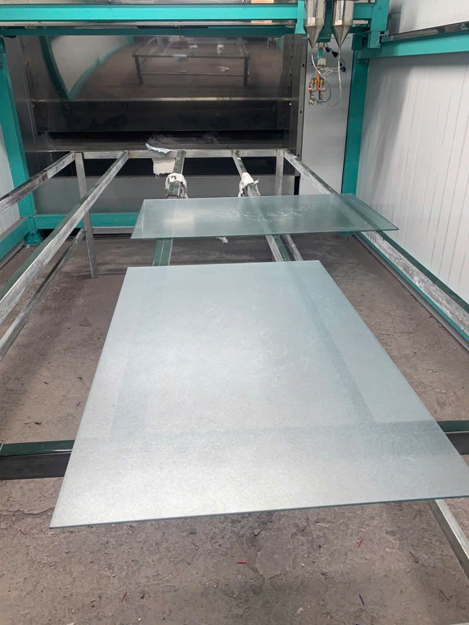 Tấm kính đặt trên bàn đỡ bên dưới cụm máy phun màu xanh