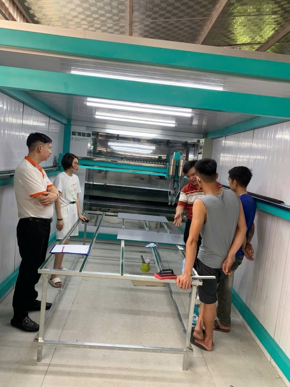 Nhóm người trao đổi bên bàn máy phun sơn trong khu vực lắp đặt