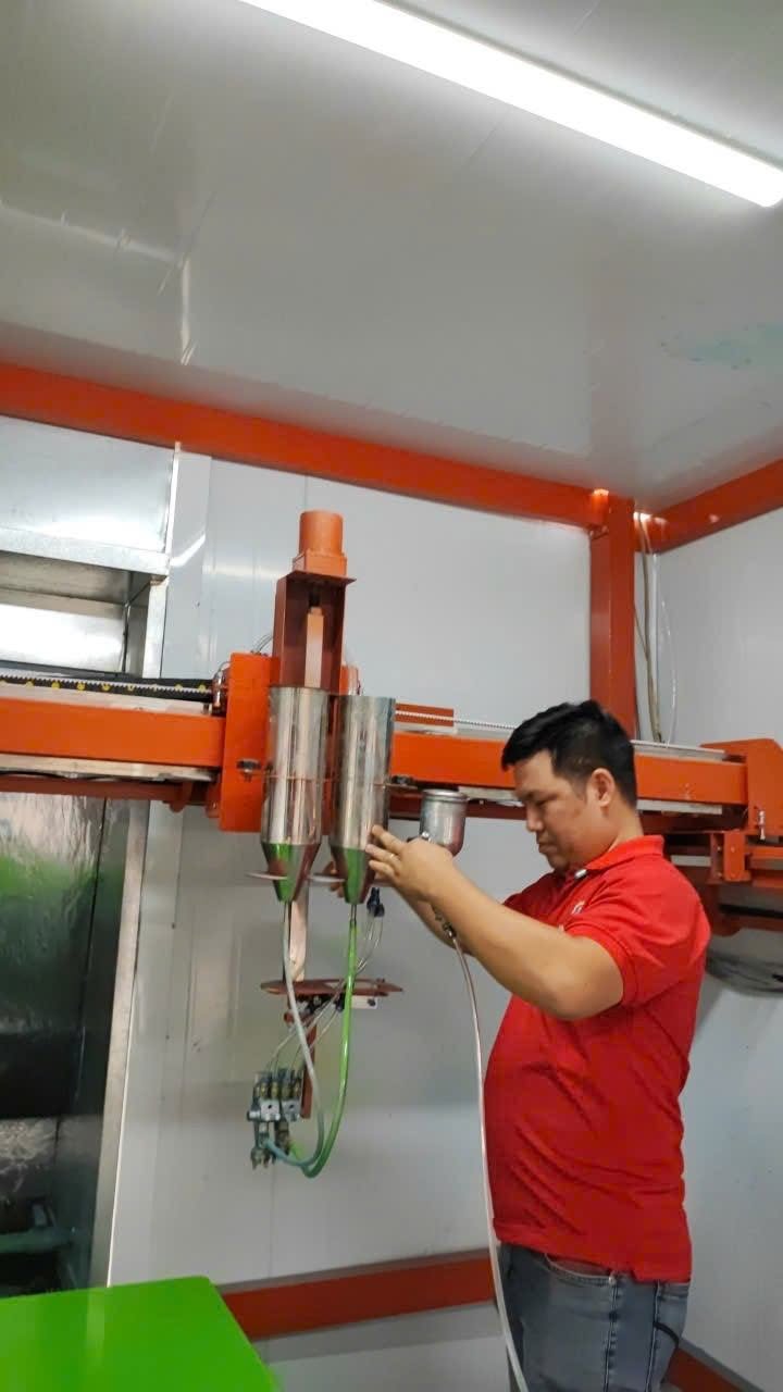 Người thao tác tại cụm cấp sơn phía trên đầu phun của máy có khung màu cam